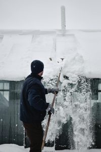 A man removes snow from a roof with a snow rake.